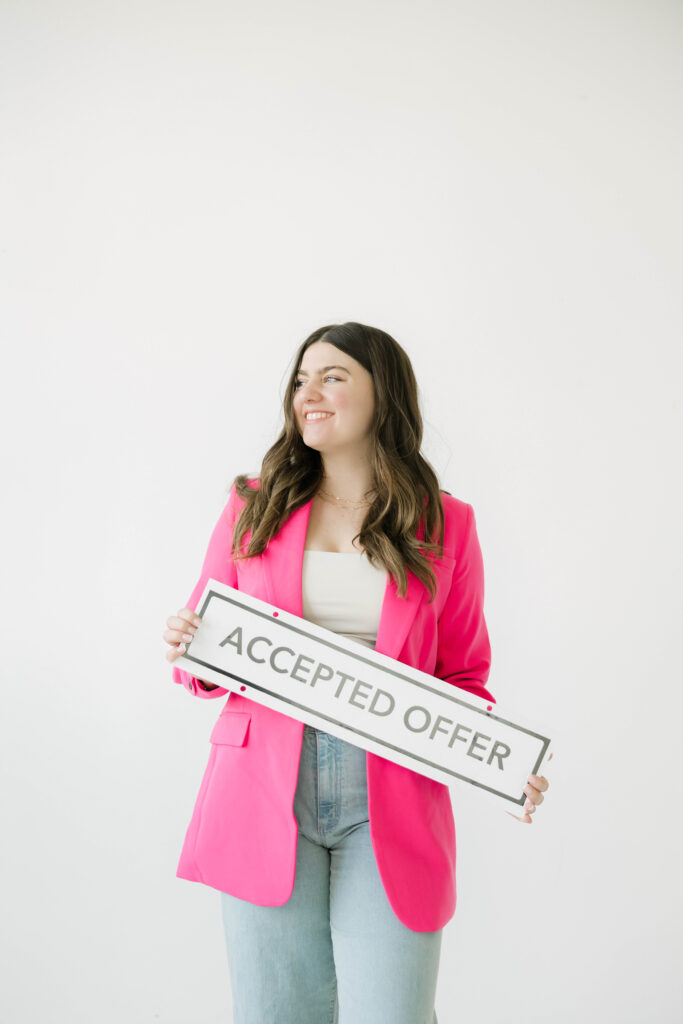 Realtor smiling during brand photoshoot holding “Accepted Offer” sign