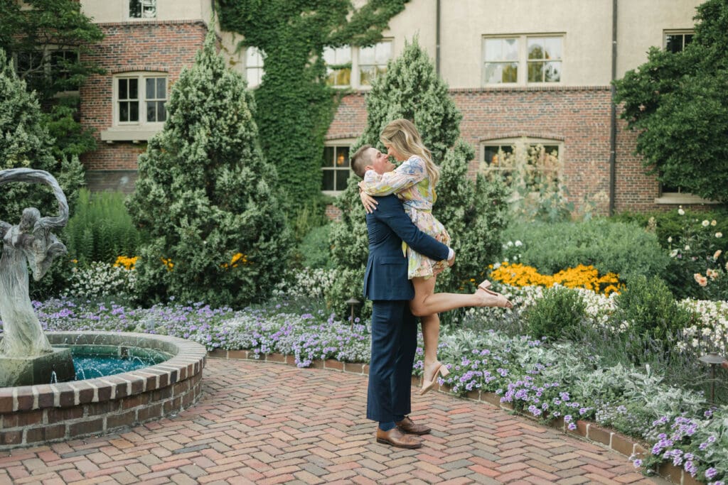 Groom-to-be lifting his fiancée in celebration during their engagement at The American Club